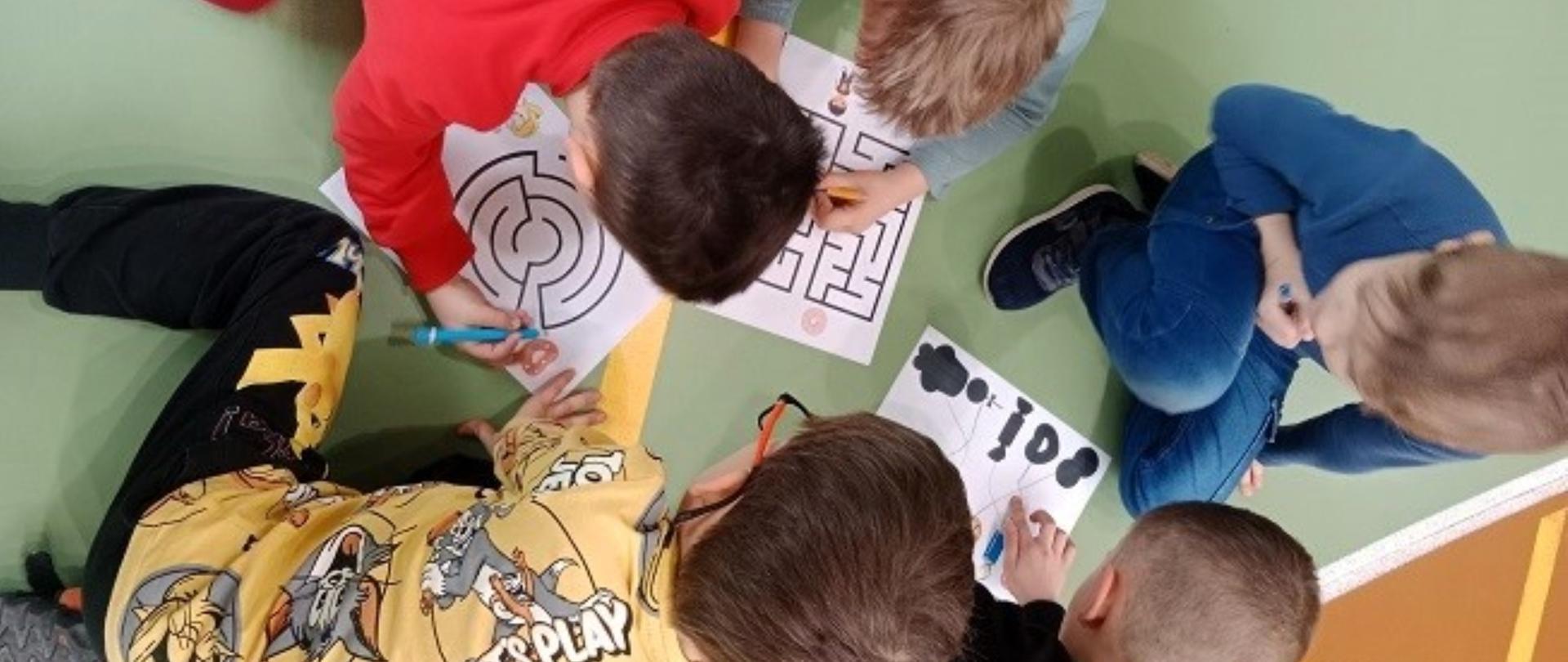 Dzieci szukają drogi w labiryncie na kartce, 4 chłopców siedzi na podłodze