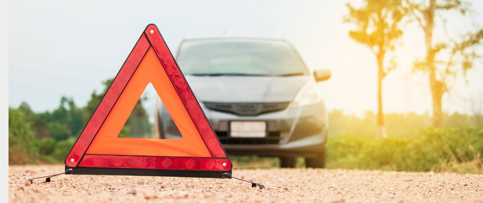 Zdjęcie trójkąta ostrzegawczego leżącego na jezdni w tle samochód osobowy