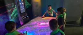 Dzieci grają w kosmiczny air hockey na świecącym, interaktywnym stole