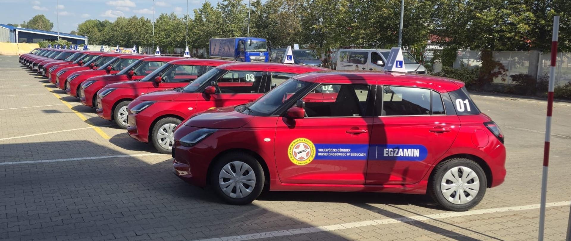 rząd czerwonych samochodów osobowych (suzuki swift) z logo WORD, Napisem EGZAMNIN i niebieskim znakiem L na dachu 