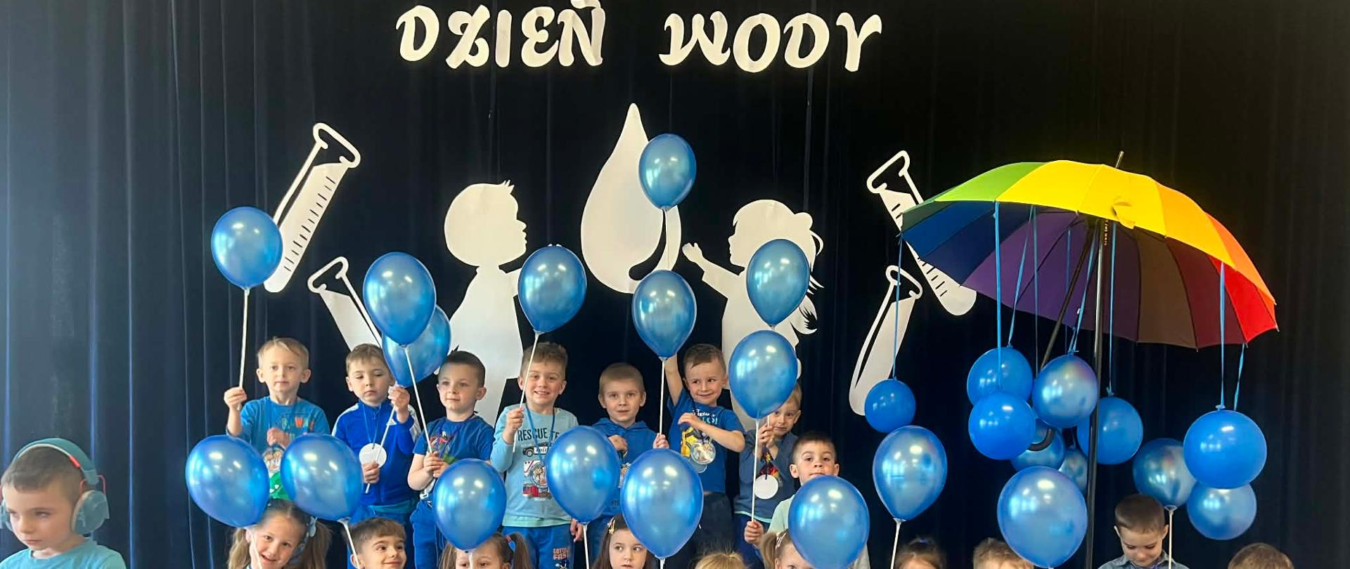 Grupa 4-latków z niebieskimi balonikami na tle dekoracji.
