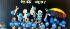 Grupa 4-latków z niebieskimi balonikami na tle dekoracji.