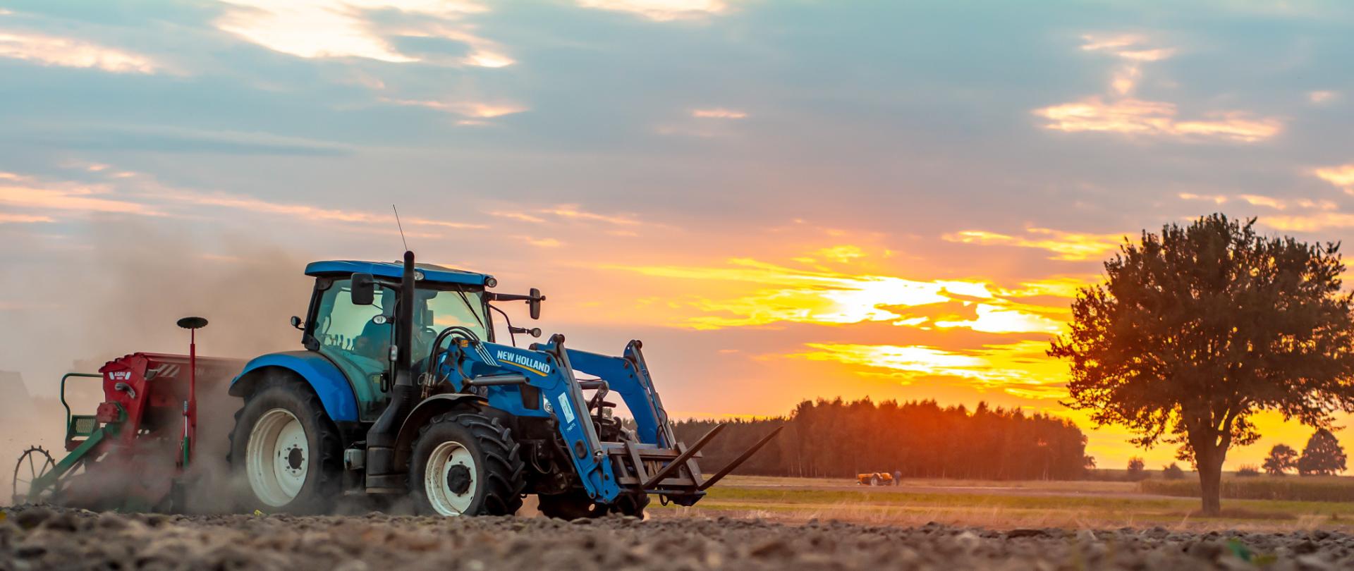 Niebieski traktor na polu o zachodzie słońca. "Płatność dla małych gospodarstw zamiast płatności bezpośrednich - oświadczenia do 31 sierpnia 2023 r."
