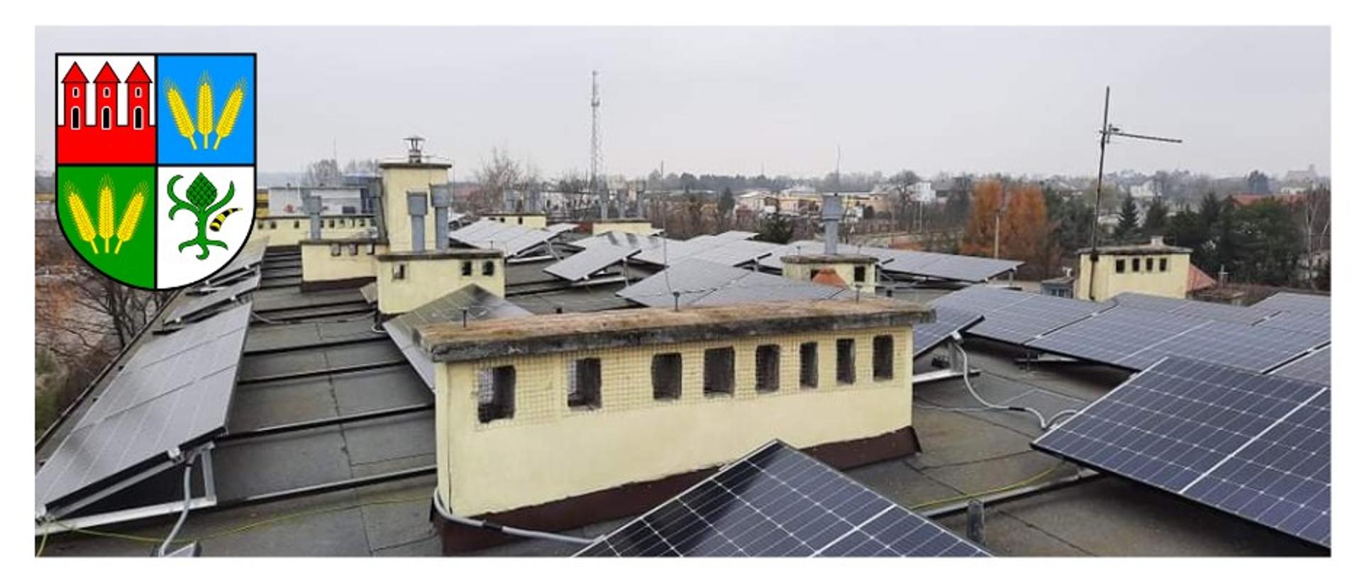 Zdjęcie przedstawia panele fotowoltaiczne zainstalowane na obiektach należących do Powiatu Przasnyskiego. W górnym lewym roku herb Powiatu Przasnyskiego.