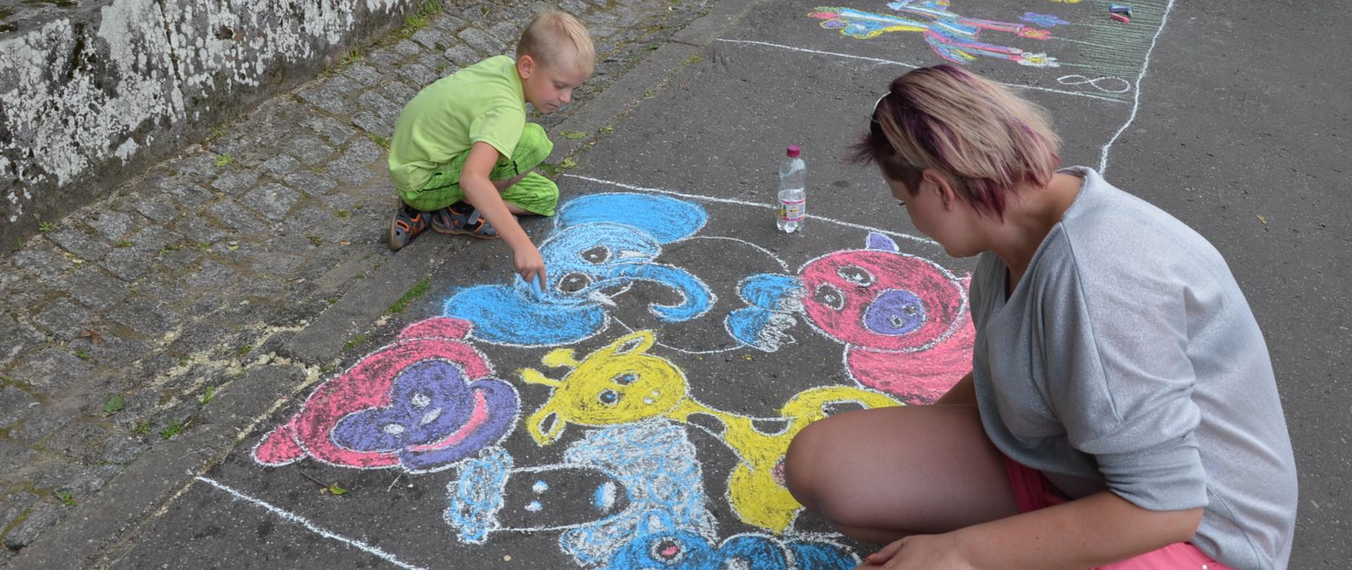 Dziecko i dorosła kobieta malują kolorowa kredą po asfalcie