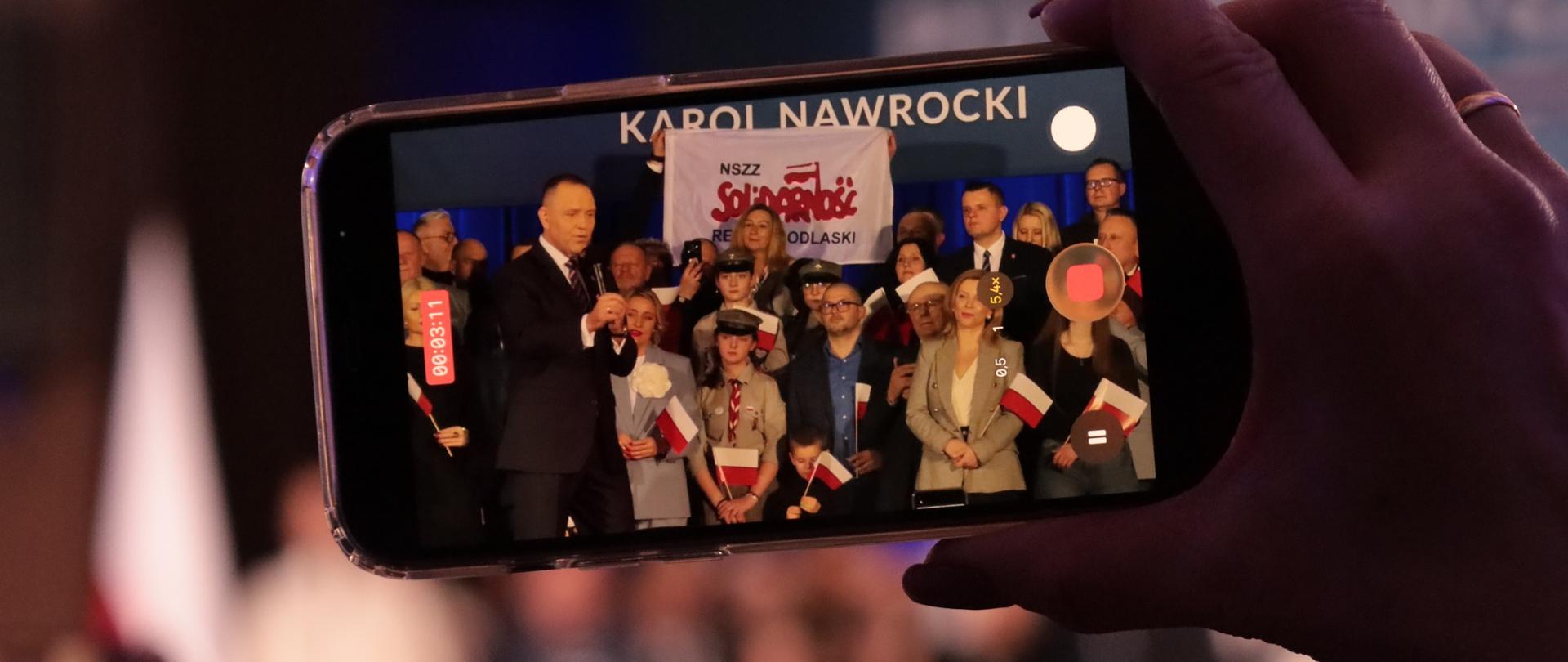 Prezydent przemawia do uczestników spotkania - widok z perspektywy smartfona