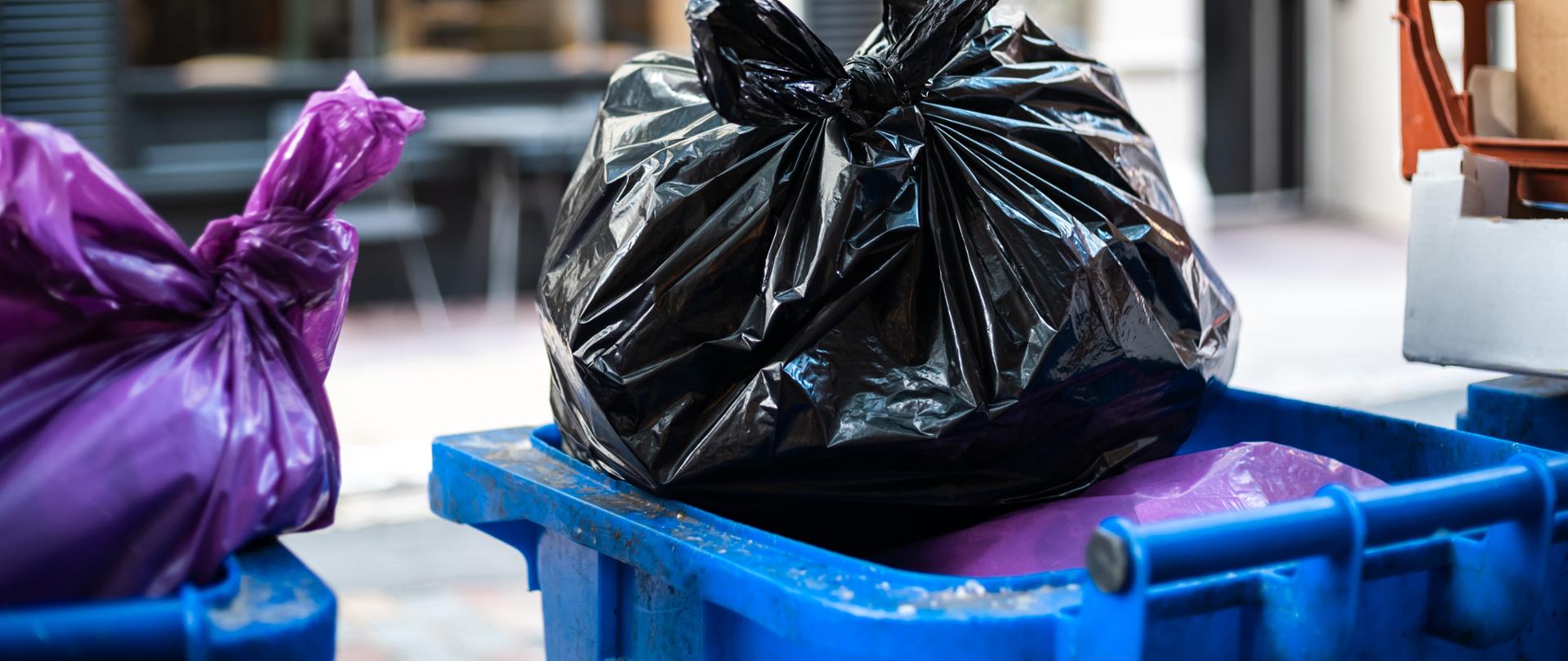 Purple and black bags of trash on a garbage bin during daytime
