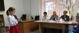 Uczestniczka konkursu przy członkach komisji i innych dzieciach czyta tekst