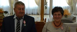 kobieta i mężczyzna ubrani w stroje galowe siedzą przy stole, uśmiechają się 