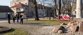 Wiceminister zdrowia, senator RP Waldemar Kraska podchodzi z wiązanka kwiatów do pomnika "Żołnierzy Niezłomnych" w kształcie krzyża z nałożoną żołnierską czapką ustawionego na kamiennej podstawie z licznymi kamieniami wokół, na których widnieją napisy upamiętniające daty, wydarzenia i osoby. Pomnik w Sokołowie Podlaskim został zbudowany w hołdzie żołnierzom Armii Krajowej i struktur poakowskich Obwodu Sokołów Podlaski, 6 Brygady Wileńskiej AK, kpt. 'Młota' oraz cywilnych mieszkańców powiatu sokołowskiego poległych w walce z komunistycznym zniewoleniem w latach 1944-1953. W tle powiewają biało czerwone flagi, widać skwer i elementy architektury miejskiej. Za senatorem stoją od lewej wicestarosta Ryszard Domański, starosta Elżbieta Sadowska, przewodniczący Rady Powiatu Sokołowskiego Jacek Odziemczyk.
