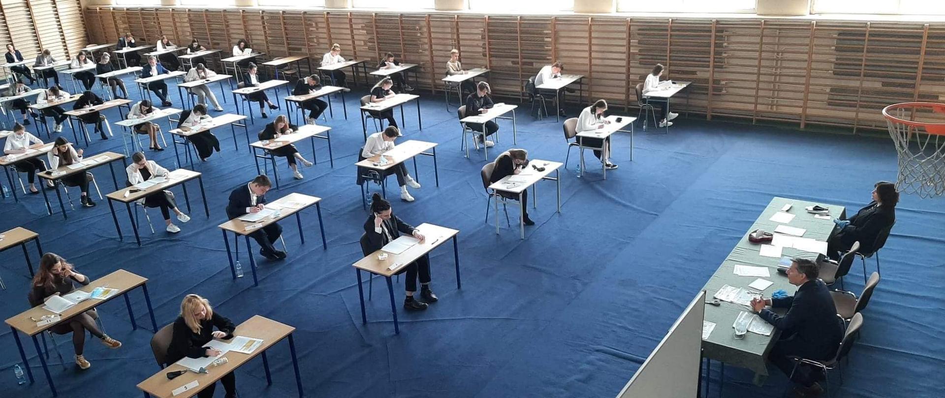 uczniowie siedzący w ławkach w pomieszczeniu