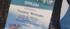 Dominika w stroju łyżwiarki trzyma dyplom za zajęcie 6 miejsca w zawodach