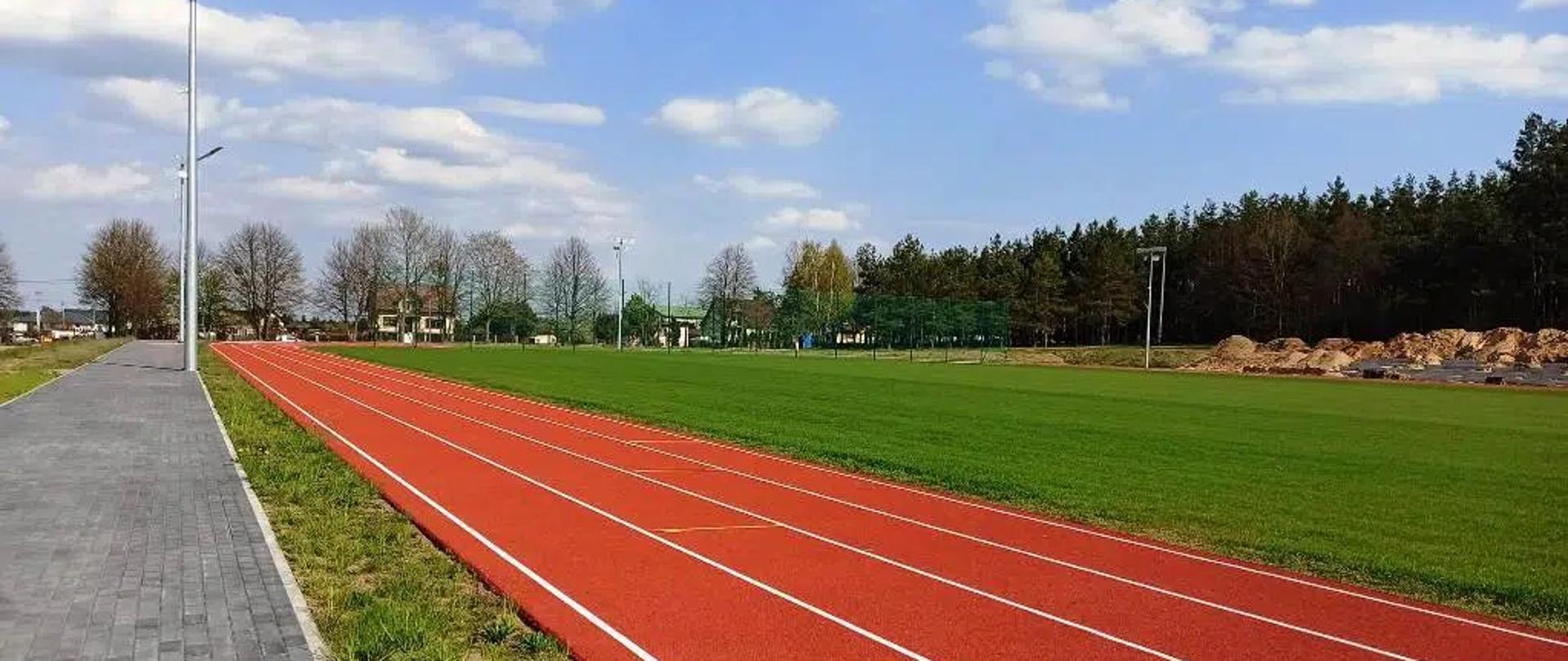 Nowo wyremontowany stadion w Jednorożcu - fragment boiska i bieżnia, w tle trwające prace nad budową trybun.