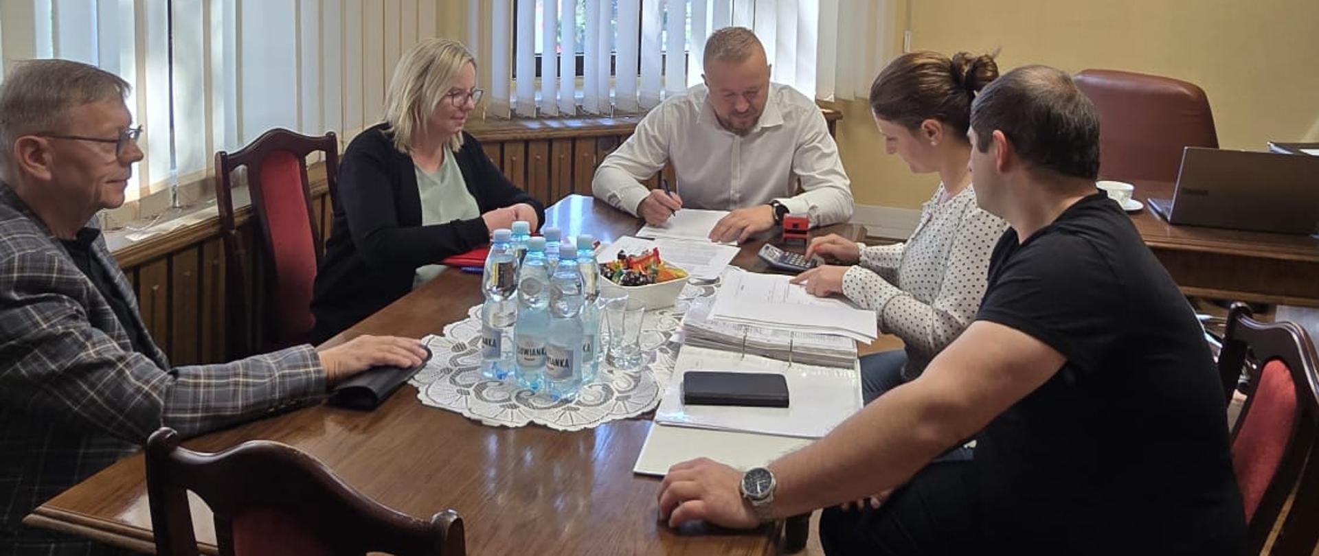 Osoby siedzące przy drewnianym stole pełnym różnych dokumentów