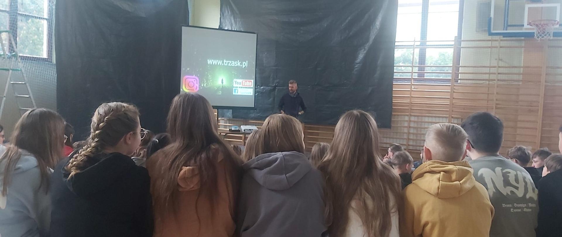 Uczniowie na hali sportowej uczestniczą w spotkaniu z podróżnikiem