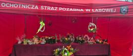 Stolik zastawiony stroikami i ciastami, nad nim czerwony namiot z napisem "Ochotnicza Straż Pożarna w Łabowej"