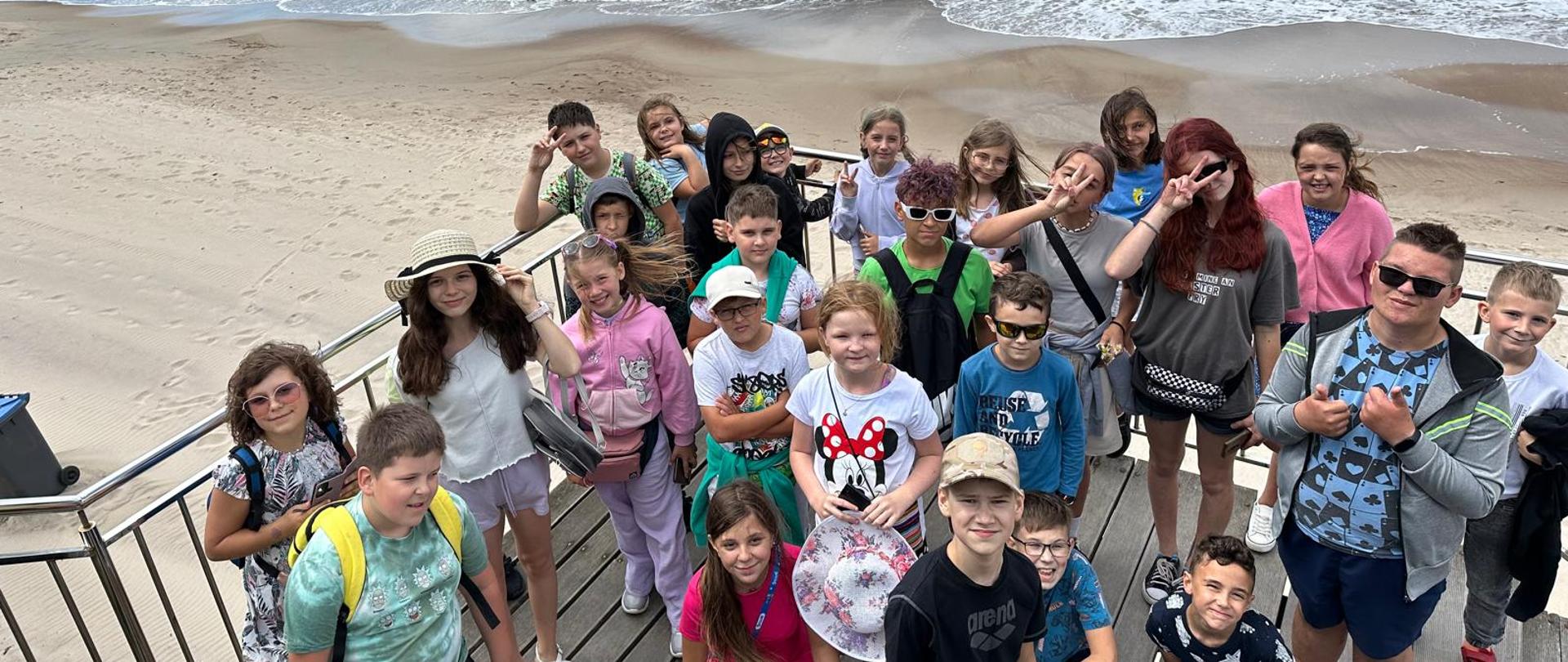 grupa młodzieży stojąca na podeście, w tle plaża i morze