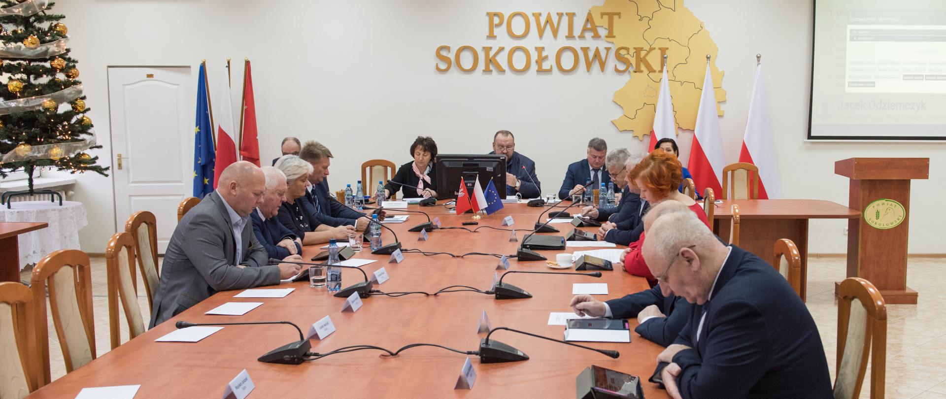 Na fotografii uwieczniony moment obrad Radnych Powiatu Sokołowskiego na LVI sesji.
Przy długim stole po prawej i lewej stronie siedzą radni, natomiast naprzeciwko przy kolejnym stole siedzą od lewej wicestarosta, starosta, przewodniczący Rady Powiatu Sokołowskiego oraz członkowie Zarządu.
Na ścianie jest napis Powiat Sokołowski wraz z krzyżem, godłem i mapą powiatu sokołowskiego, po prawej stronie widnieją wyniki z głosowania radnych.