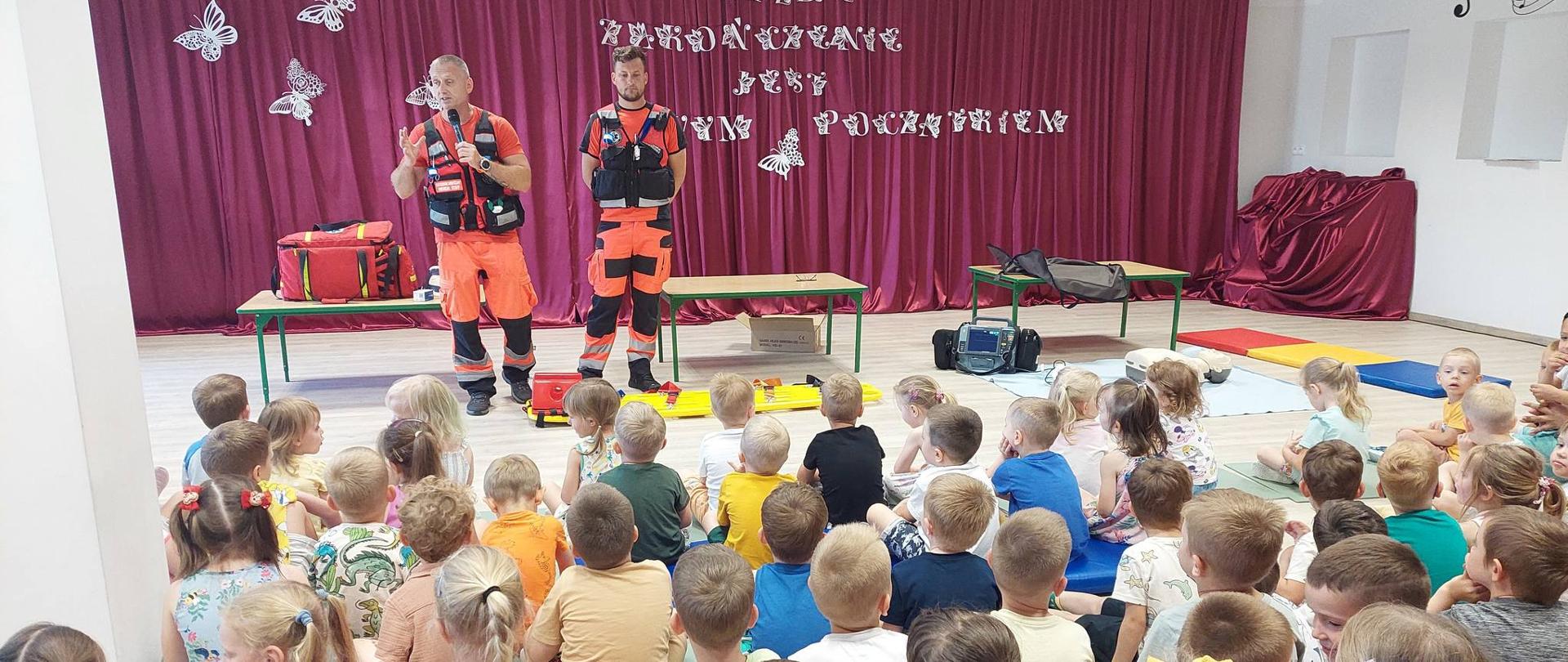 2 ratowników medycznych stoją przed dziećmi