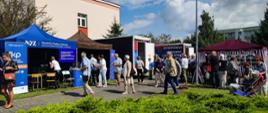 Festyn Profilaktyczno Zdrowotny w ogrodach przasnyskiego szpitala. Zdjęcie przedstawia uczestników Festynu zasięgających porad przy stanowiskach: Narodowego Funduszu Zdrowia, Caritasu, Ostebusa i Dermatobusa.