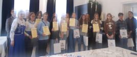 grupowe zdjęcie wszystkich uczestników zmagań konkursowych, na fotografii stoi kilkanaście osób, uczniowie trzymają w rękach dyplomy oraz otrzymane nagrody.