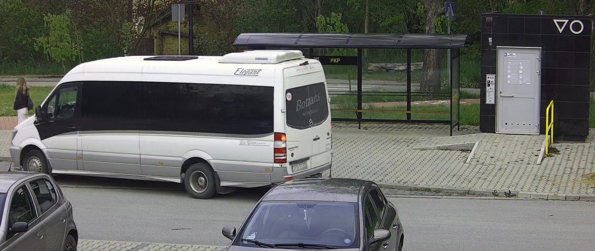 Szary bus wjeżdżający na przystanek autobusowy. W tle zielone drzewa.