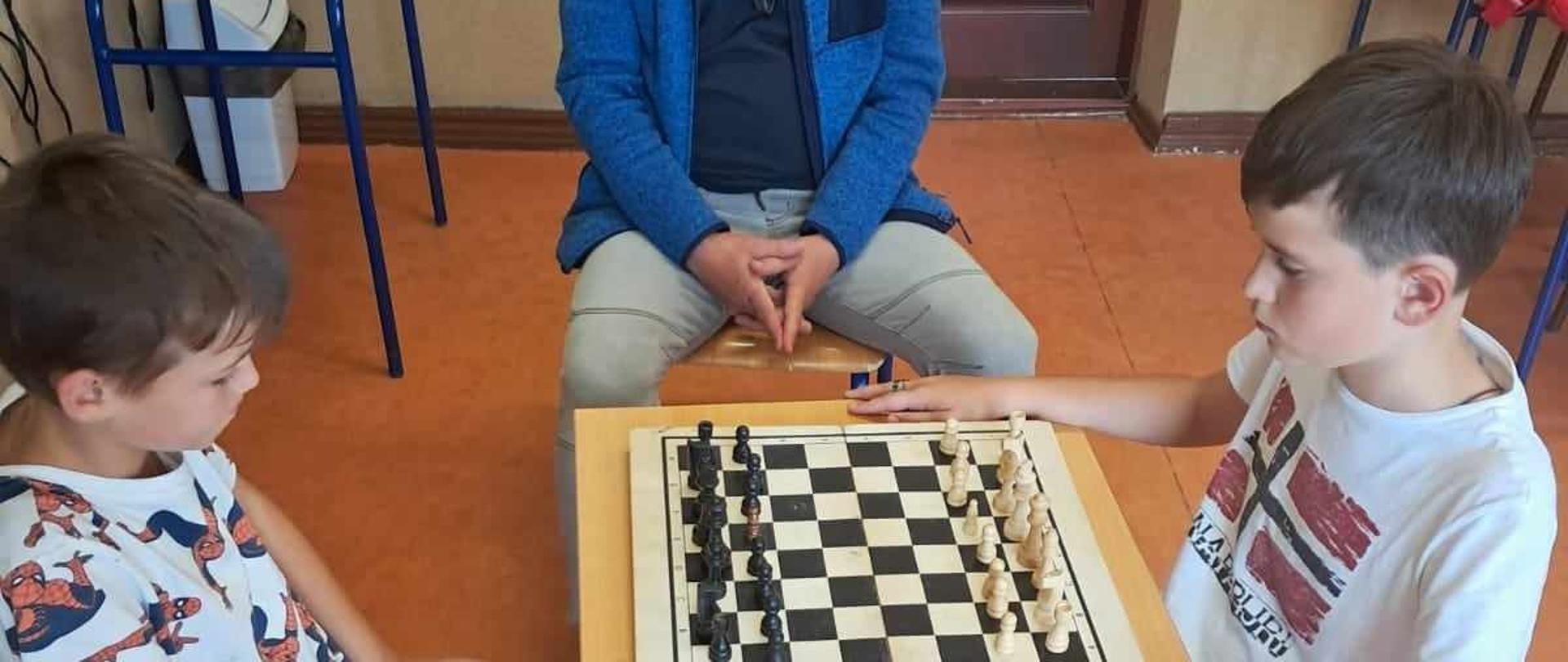 Uczniowie prowadzą rozgrywki szachowe, nad przebiegiem których czuwa sędzia 