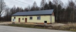 Zdjęcie przedstawia budynek w gorszym stanie technicznym i z mniejszym trawnikiem. Elewacja jest zniszczona a okna i drzwi są starsze. W tle widać drzewa i niebo.