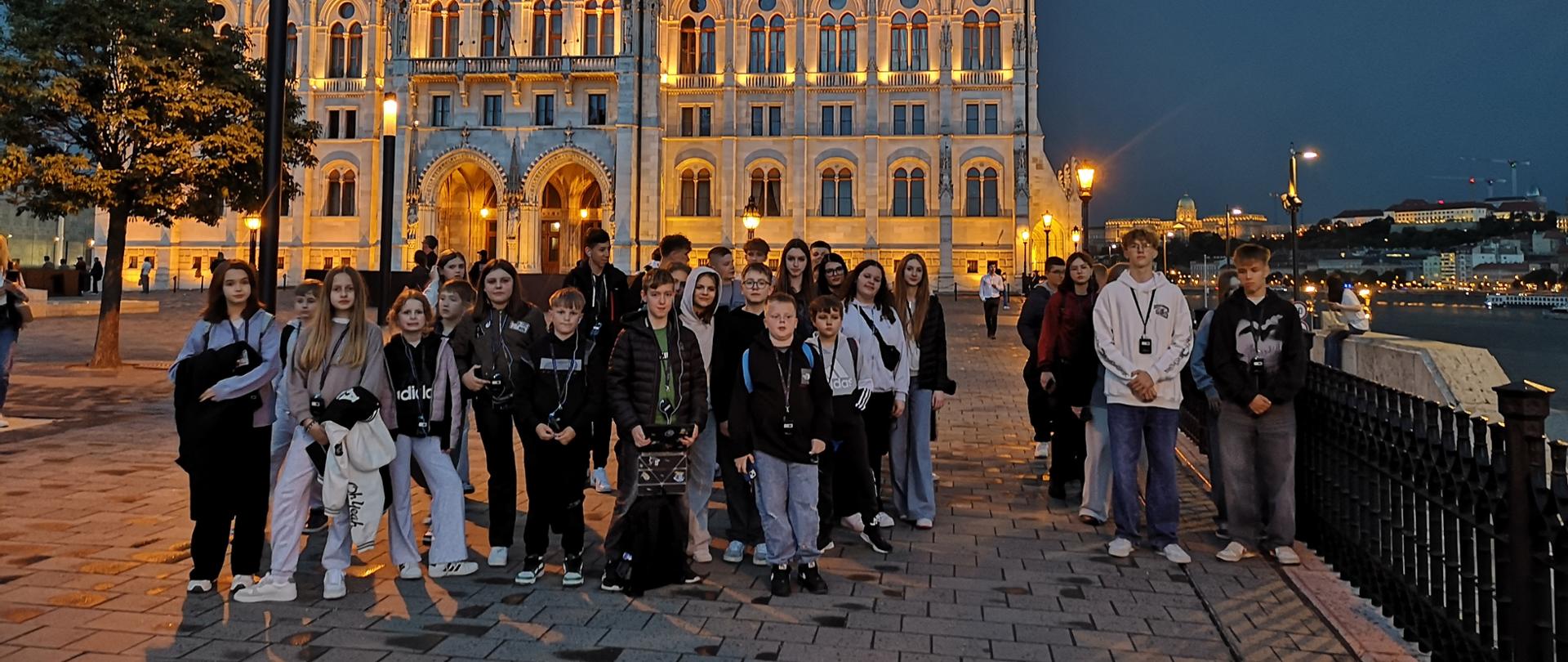 Zdjęcie grupowe wykonane nocą w tle oświetlony budynek