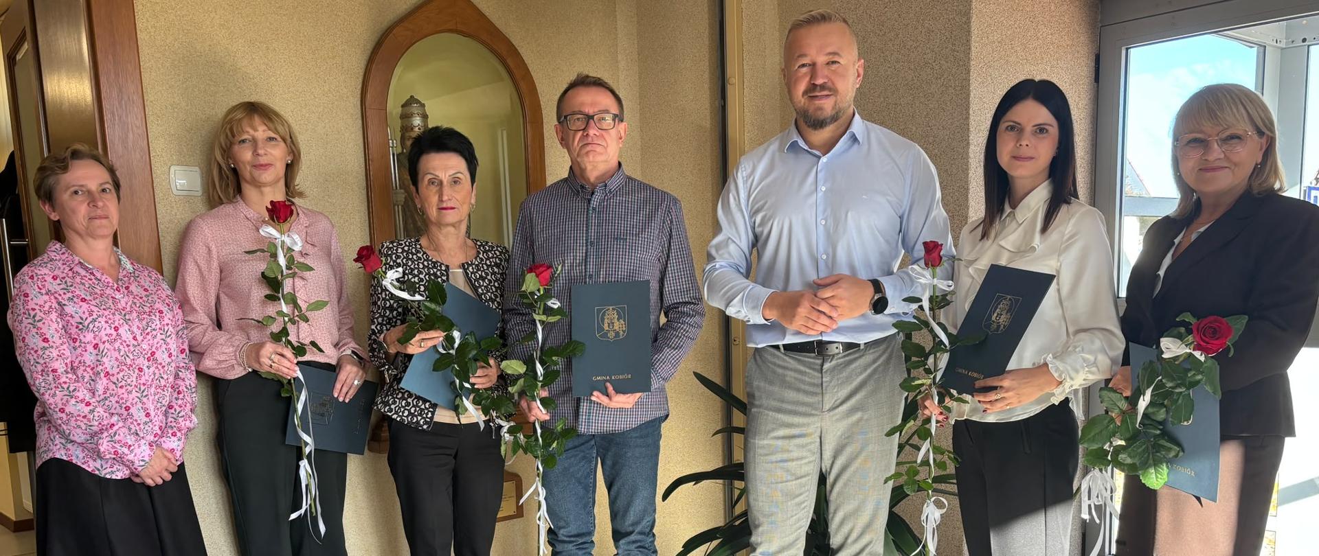 Wójt Gminy Kobiór wraz z dyrekcją i nauczycielami szkoły oraz przedszkola, którzy otrzymali Nagrody Wójta. Wyróżnieni trzymają pamiątkowe dyplomy i czerwone róże.