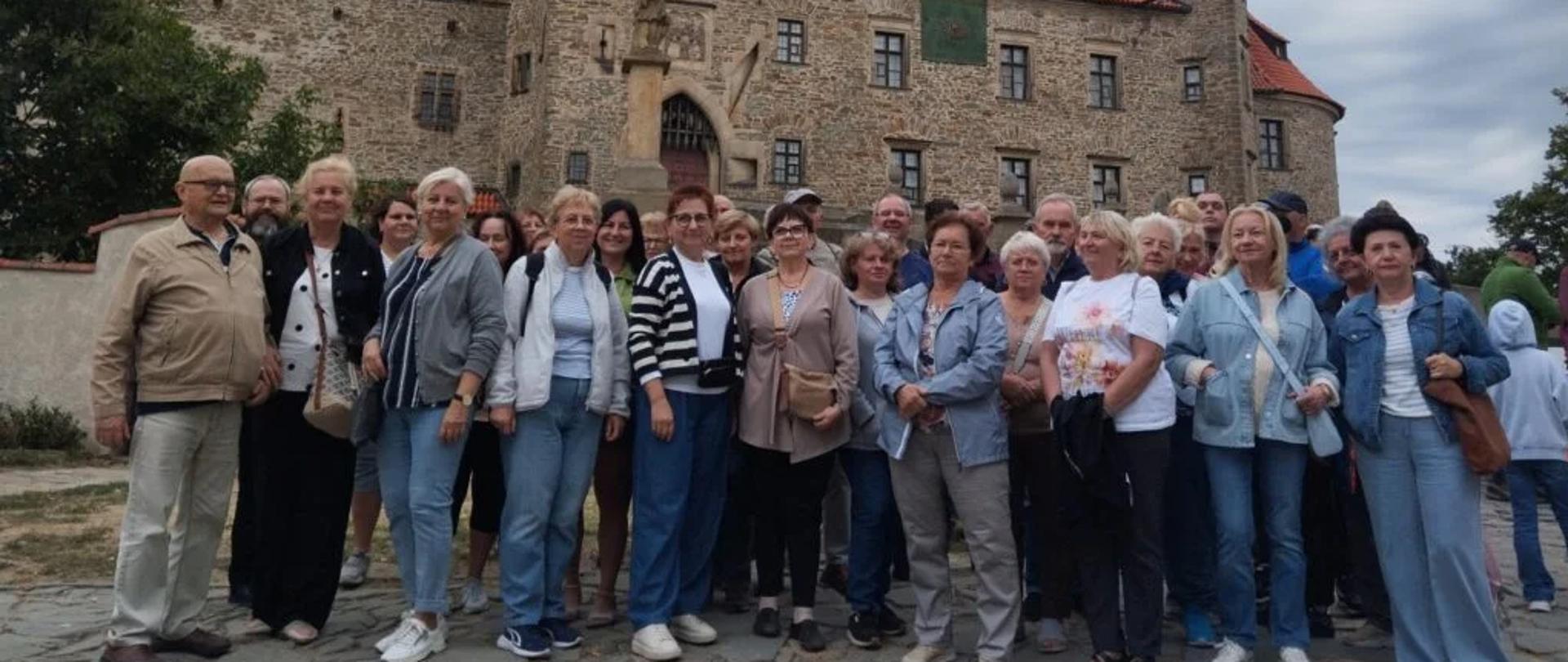 Grupa ludzi pozuje do zdjęcia przed kamiennym zamkiem