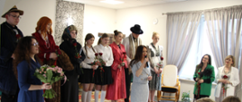Grupa teatralna z ZS1 na scenie w przeróżnych strojach. Przed nimi stoi starosta zambrowski Pani Edyta Marchelska-Groszfeld, która przemawia do mikrofonu, a obok niej stoją opiekunki grupy teatralnej, które wraz z aktorami trzymają czerwone róże.