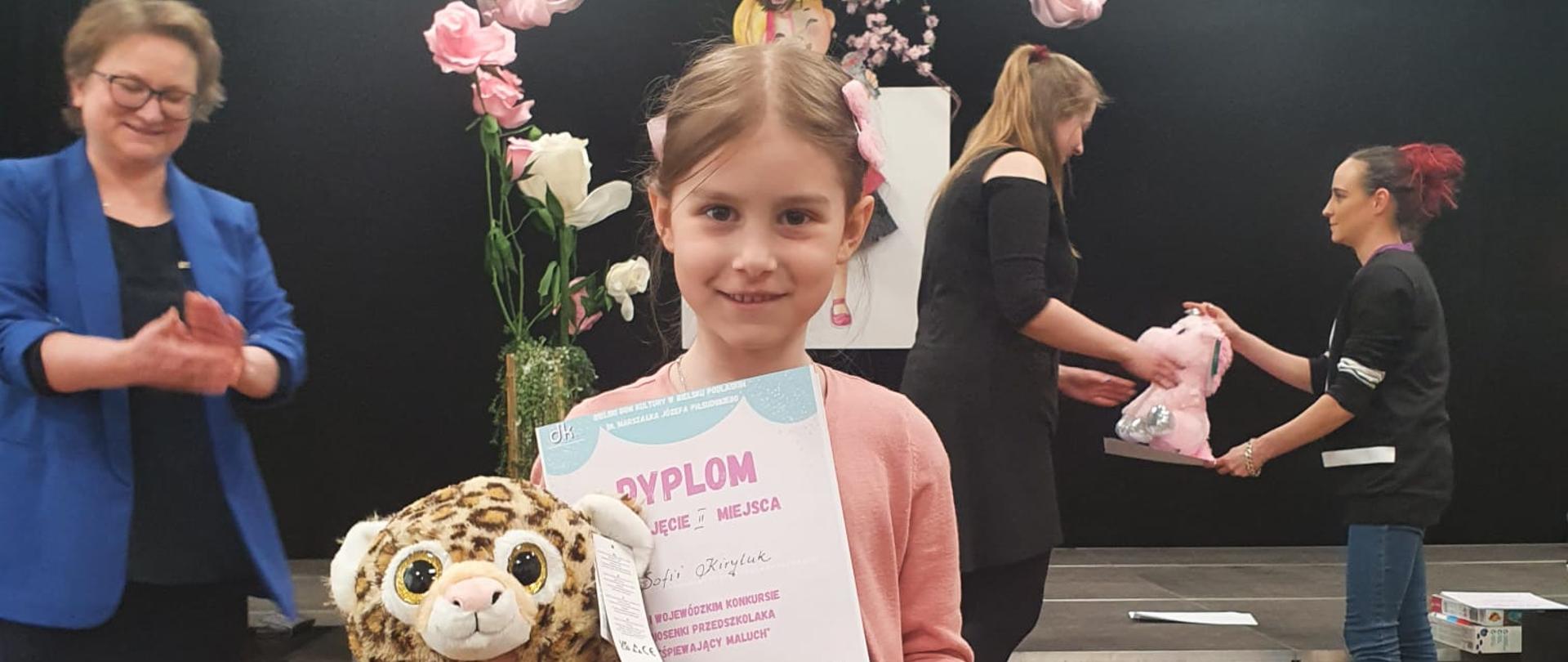 Młoda solistka prezentuje dyplom i otrzymaną maskotkę 