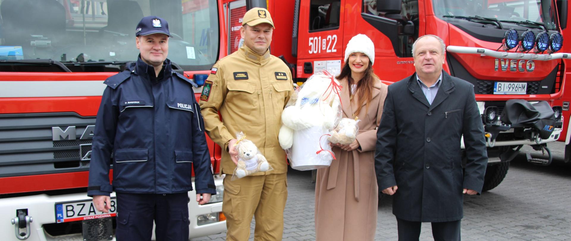 Zdjęcie przedstawia przekazanie pluszaków dla dzieci poszkodowanych w wypadkach. Uroczystość odbyła się na placu przed Komendą Powiatową Państwowej Straży Pożarnej w Zambrowie.
Na zdjęciu widoczni są: Zastępca Komendanta Powiatowego Policji w Zambrowie, Komendant Powiatowy Państwowej Straży Pożarnej w Zambrowie, Starosta Zambrowski Edyta Marchelska-Groszfeld i Wicestarosta Zambrowski Robert Maciej Rosiak.
Pluszaki ufundowane przez starostę, wicestarostę i zastępcę komendanta policji mają służyć jako wsparcie psychologiczne dla dzieci, które ucierpiały w zdarzeniach losowych, zwłaszcza wypadkach drogowych.
