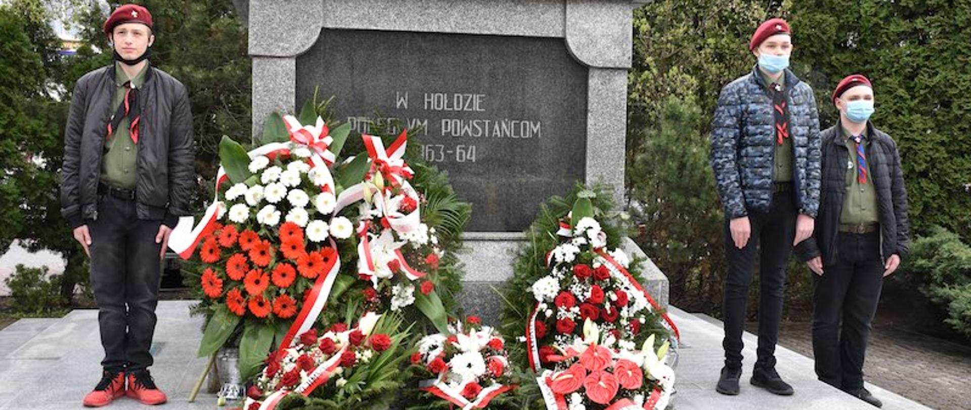 na zdjęciu znajduje się pomnik Powstania Styczniowego w Zambrowie, a przy nim stoją harcerze, którzy pełnią wartę oraz 6 wiązanki kwiatów