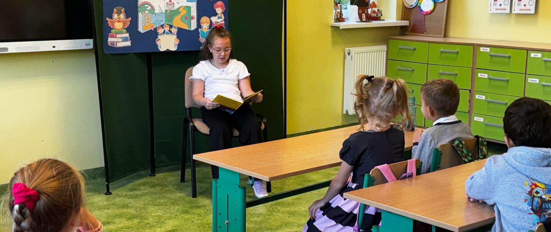 Dziewczynka na krześle czyta książkę dla pozostałych uczniów w klasie