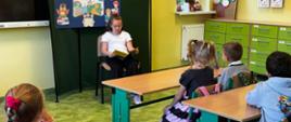 Dziewczynka na krześle czyta książkę dla pozostałych uczniów w klasie