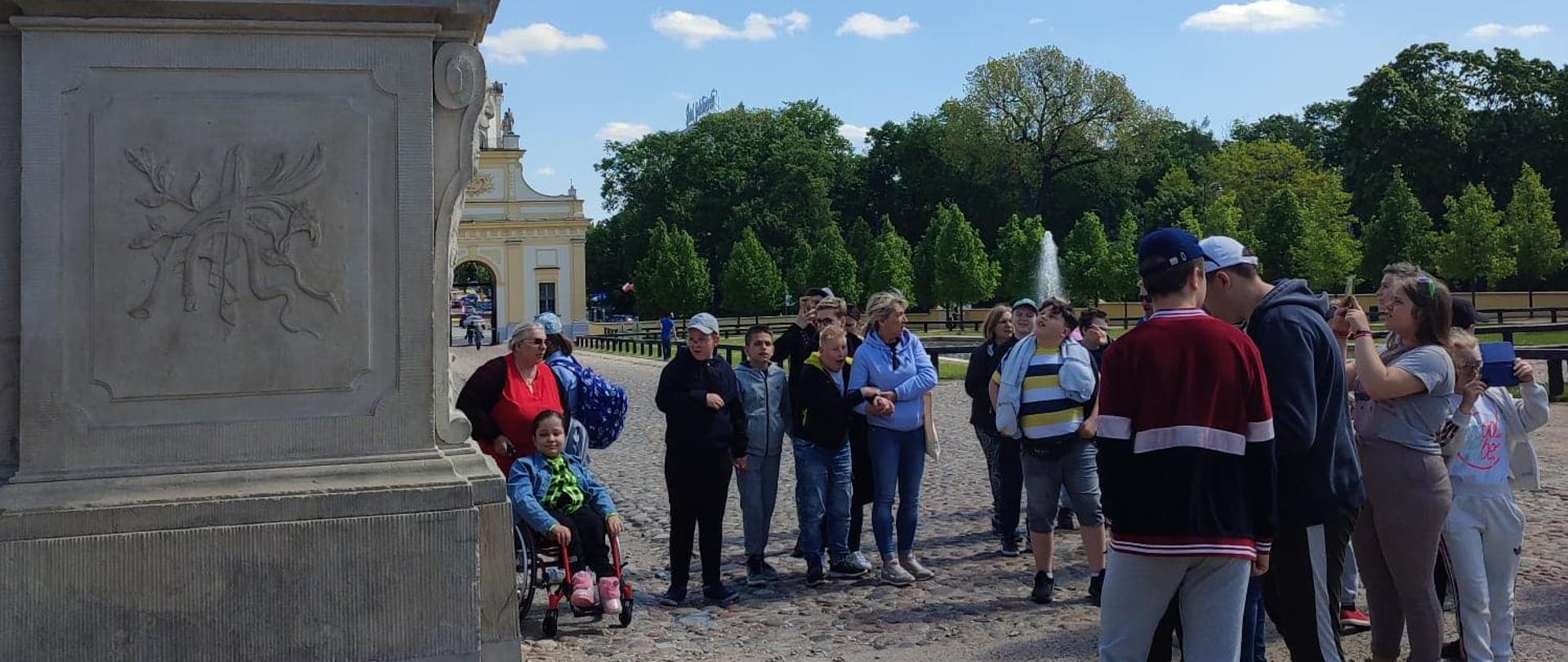 Na zdjęciu widoczna jest grupa dzieci i młodzieży stojąca pod pomnikiem