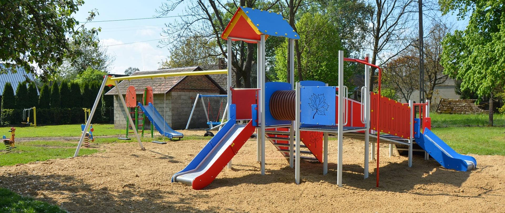 urządzenie zabawowe na placu piaszczystym podłożu, zjeżdżalnia, czerwone drabinki, huśtawki