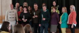 Organizatorzy i nauczyciele trzymający statuetki na pamiątkowym zdjęciu
