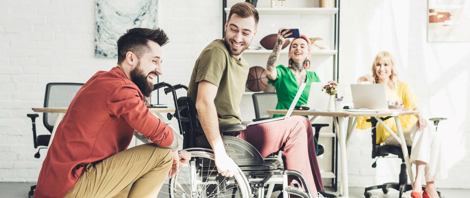 Zdjęcie grupy młodych osób w biurze, jedna z nich siedzi na wózku inwalidzkim