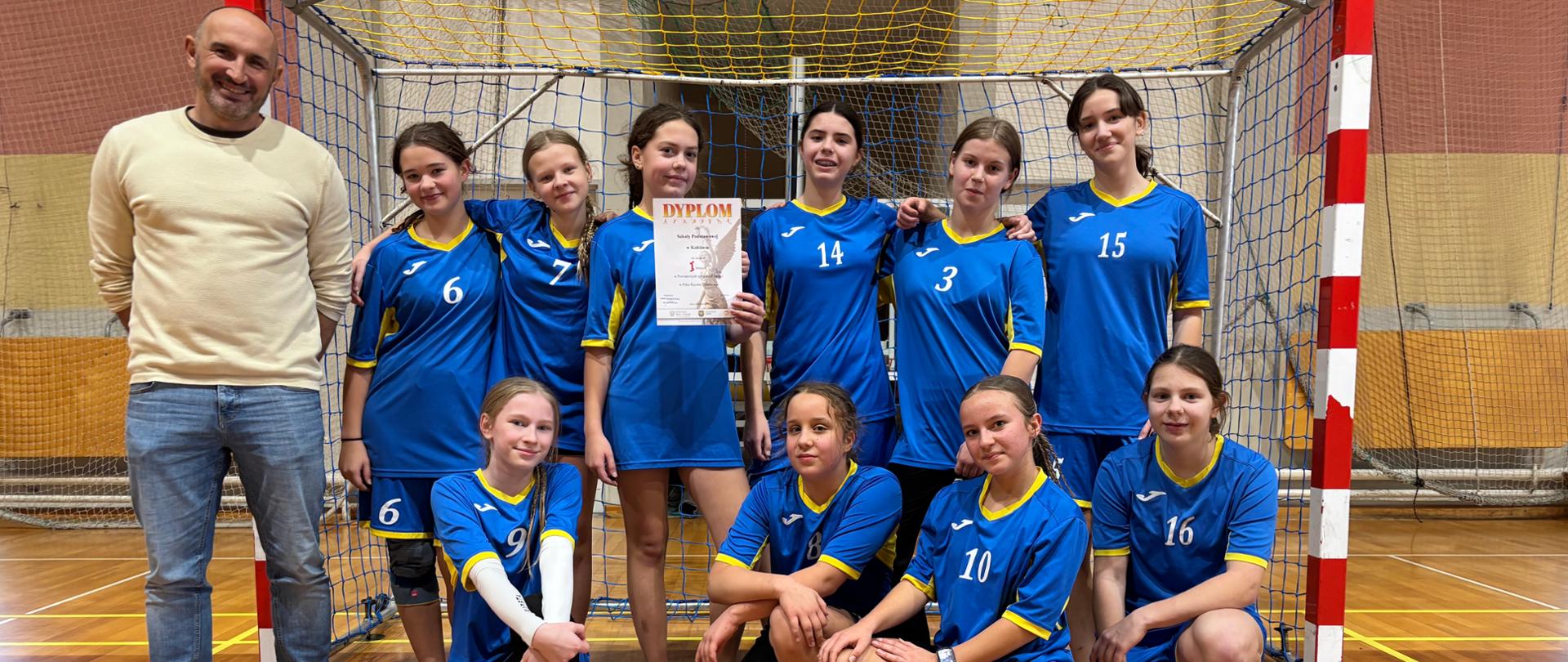 Dziewczyny w niebieskich sportowych strojach z opiekunem pozują do zdjęcia w hali sportowej