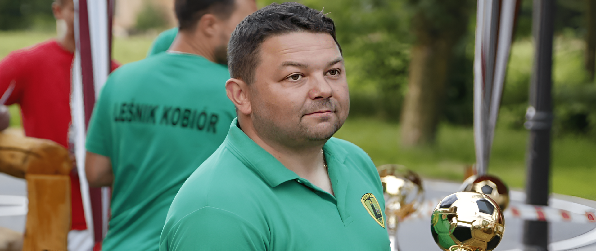 Mężczyzna w zielonej koszulce obok złote puchary w kształcie piłki