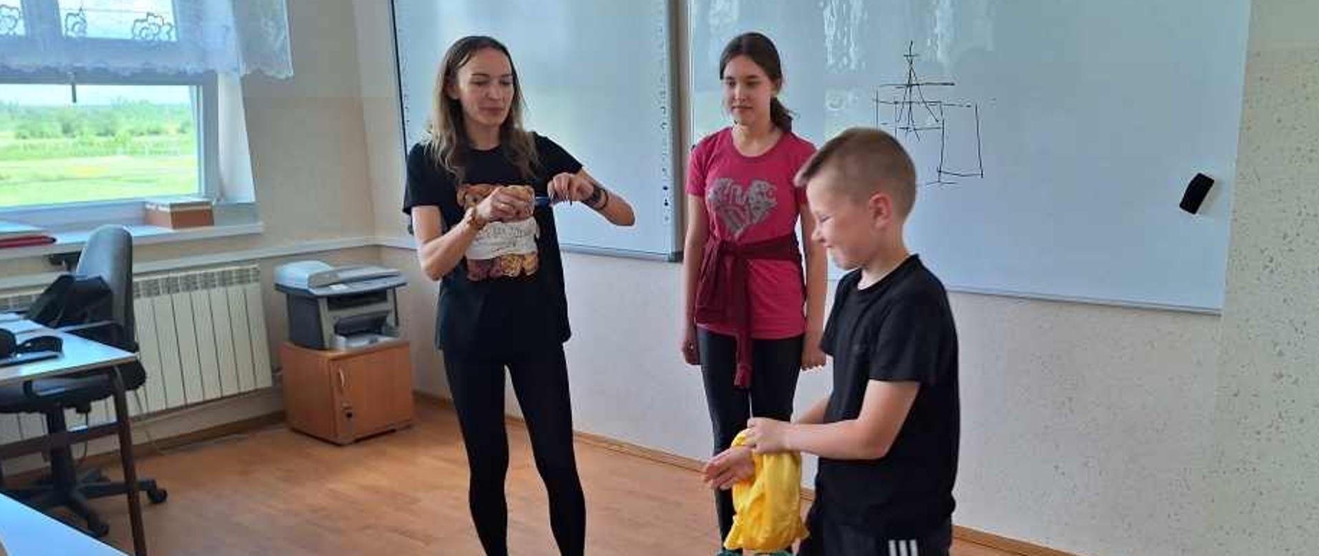 Uczniowie na sali lekcyjnej wraz z prowadzącą wykonują ćwiczenia.