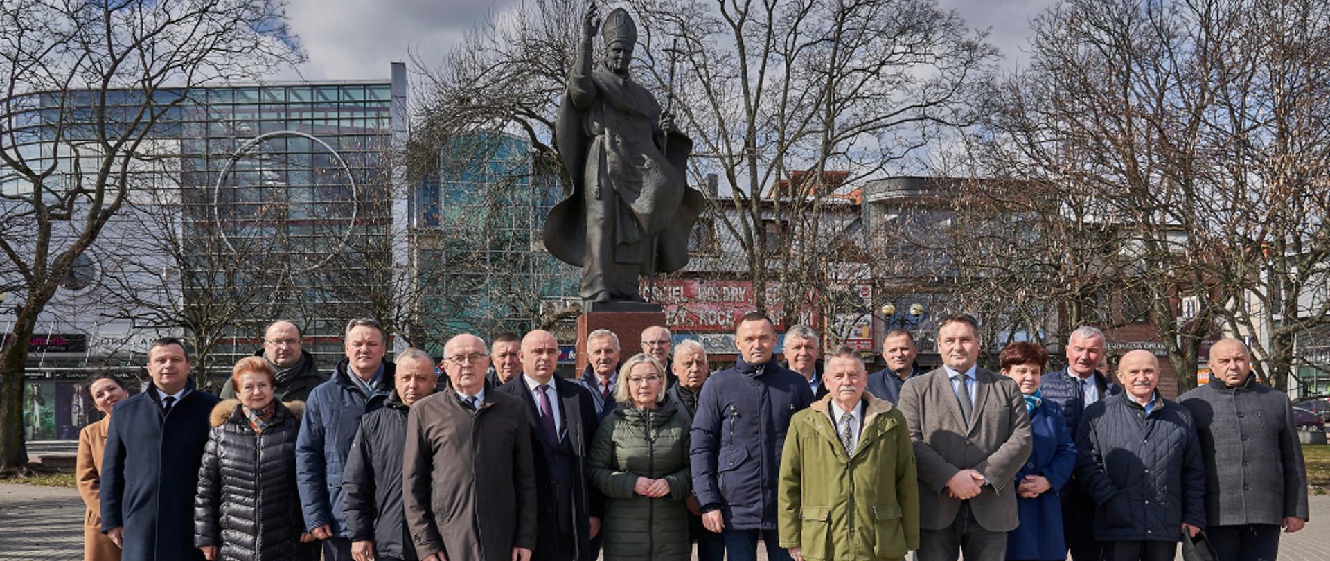 Grafika przedstawia: Radni Powiatu Siedleckiego i członkowie Zarządu Powiatu pod pomnikiem papieża Jana Pawła II w Siedlcach