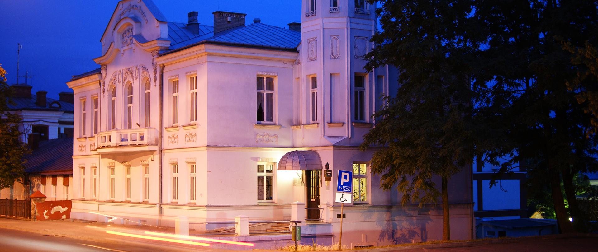 Zdjęcie przedstawia biały, oświetlony budynek w nocy