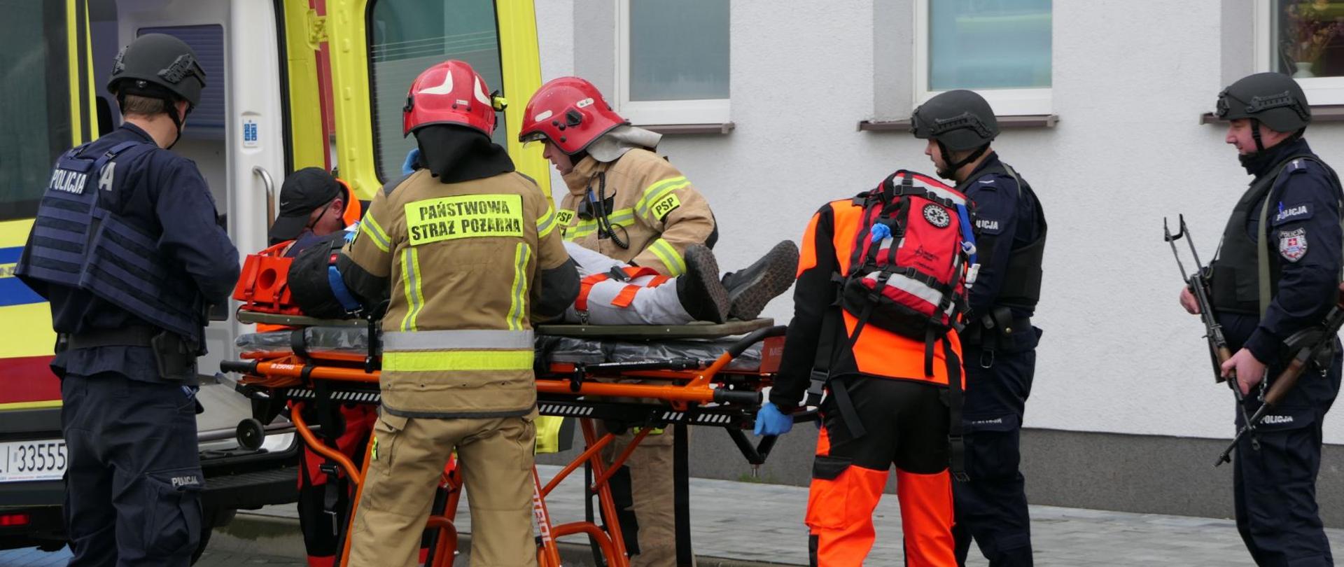 Inscenizacja szkoleniowa z udziałem funkcjonariuszy policji, straży i służby medycznej. Transport poszkodowanego do Ambulansu.