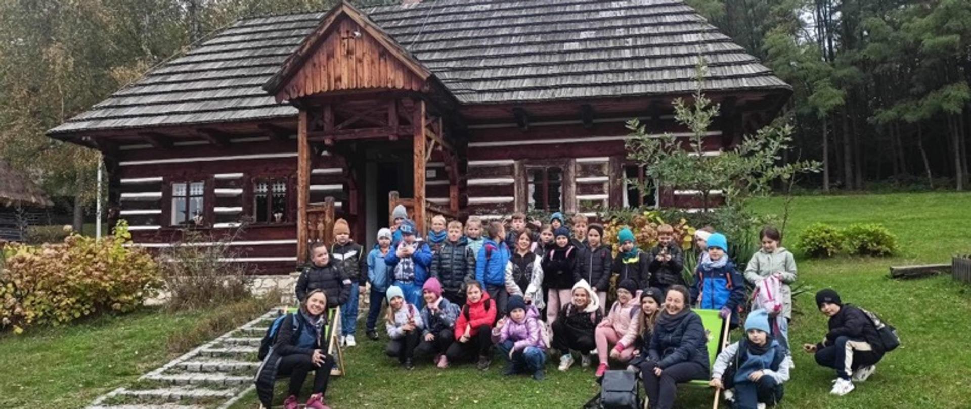 Na zdjęciu widać grupę dzieci z wychowawczyniami na tle starego, drewnianego domu.