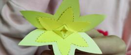 Kwiat wykonany z papieru w dłoniach dziewczynki w różowej bluzie