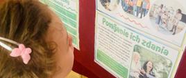 Uczennica w białym podkoszulku czyta informacje na temat Osób Niepełnosprawnych zamieszczone na gazetce informacyjnej. Na gazetce widoczna zielona, czerwona i żółta grafika informacyjna oraz zdjęcia Osób Niepełnosprawnych zamieszczone w kolistych lub kwadratowych okienkach